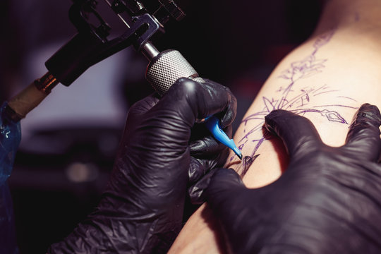 Close up of the tattoo artist hands creating a tattoo on a girl's arm