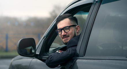 Portrait of successful business man in glasses sitting at the wheel of an expensive car and looking out the door window