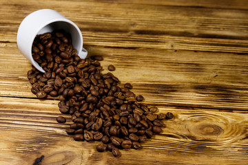 Roasted coffee beans spill out of cup on wooden table