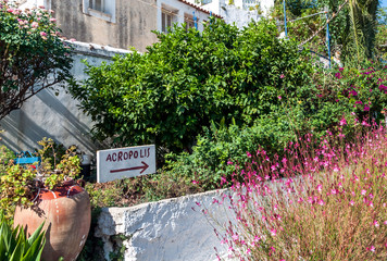 The old handmade signpost standing beetween garden flowers and pointing to the Acropolis in Athens, Greece