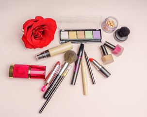 Obraz na płótnie Canvas The composition of accessories, makeup cosmetics on a soft pink background with a beautiful red rose flower. Top view. 