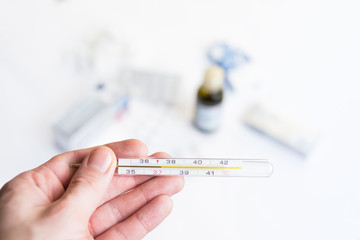Hand holding a thermometer with pills and medications on background