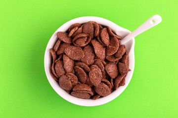 Crunchy chocolate corn flakes in bowl on bright green background