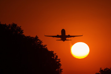 Silhouette of an air plane near to the sun with beautiful red clouds in background