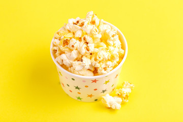 Tasty salty popcorn in paper cup on bright yellow backgraund