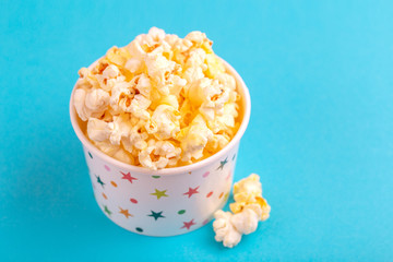 Tasty salty popcorn in paper cup on bright blue backgraund