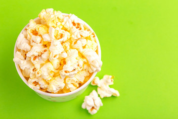 Tasty salty popcorn in paper cup on bright green backgraund