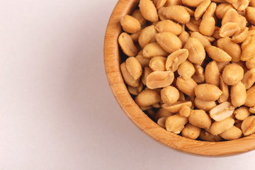 Roasted peanuts in wooden bowl on light marble background