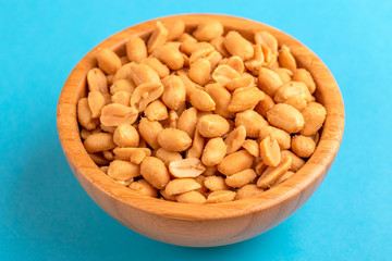 Roasted peanuts in wooden bowl on bright blue background