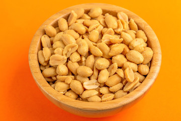 Roasted peanuts in wooden bowl on bright orange background