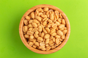 Roasted peanuts in wooden bowl on bright green background