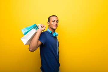 African american man with blue t-shirt on yellow background holding a lot of shopping bags