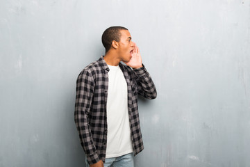 Young african american man with checkered shirt shouting with mouth wide open to the lateral