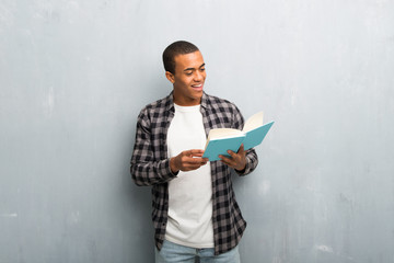 Young african american man with checkered shirt holding a book and enjoying reading