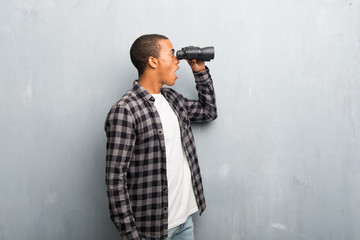 Young african american man with checkered shirt and looking for something in the distance with binoculars