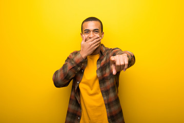 Young african american man on vibrant yellow background pointing with finger at someone and laughing