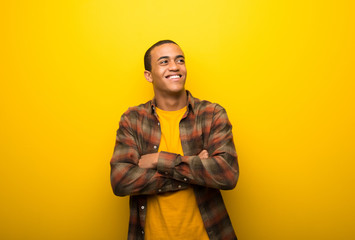 Young african american man on vibrant yellow background looking up while smiling