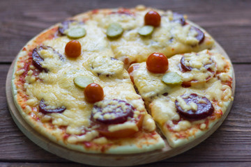 homemade hot pizza with salami and cheese, pickles and tomatoes on wooden background, ready to eat