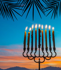 Burning candles in menorah are traditional symbols for Hebrew celebration of Hanukkah holiday. Background of sunrise and night mountain sky, selective focus on menorah