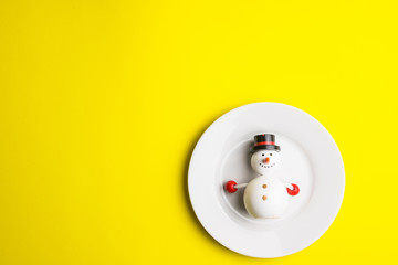Small snowman on white dish isolated on yellow background at Christmas day.Theme Christmas day background.