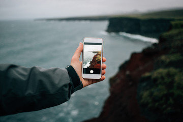 Adventurer, hiker or tourist holds out smartphone with photograph of amazing epic rough and beautiful icelandic landscape. Travel blogger or social media influencer explores place less travelled © BublikHaus