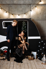 The concept of the Christmas party. Stylish couple in love in black man and woman hugging on the background of dark Christmas decor.