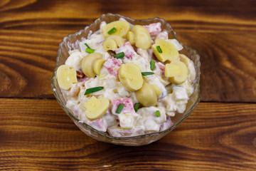 Potato salad with marinated mushrooms, sausage, onion and mayonnaise on wooden table