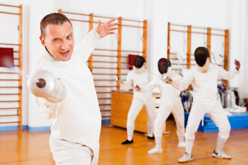 Sporty young man fencer practicing effective fencing techniques in training room