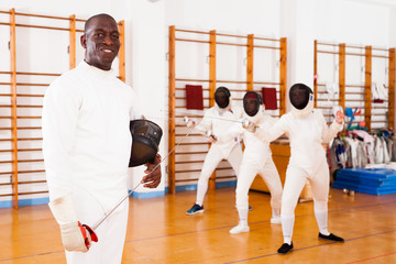 African american male fencer in uniform standing with mask and foil