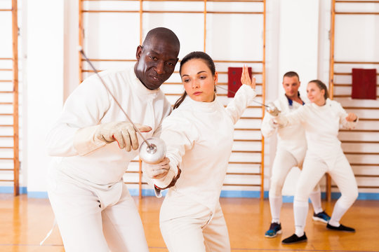 Female fencer practicing movements with african american male trainer - Powered by Adobe