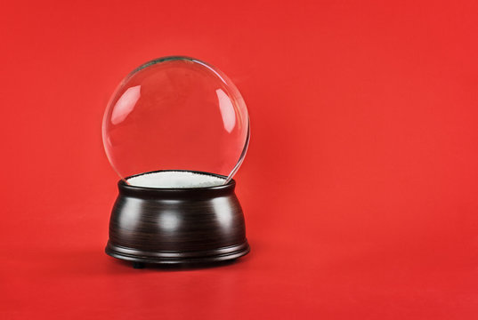 Empty glass snow globe with wooden base against a red background. Free copy space for text included.