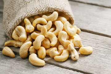 Cashew nuts in burlap bag on wooden gray background . Healthy food
