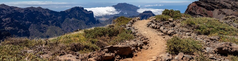 Mountain path close up leading to a cliff. Background volcano and blue clouds.