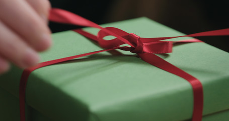 Macro shot of female hands tying red ribbon bow on green paper gift box