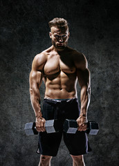 Fototapeta na wymiar Young guy working out with dumbbells. Photo of strong male with naked torso on dark background. Strength and motivation