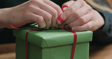 Closeup shot of female hands tying red ribbon bow on green paper gift box