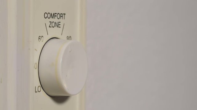 A hand turning on and adjusting the home heater temperature on a wall mounted control knob,