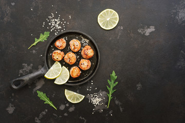 Scallops fried in a pan with lemon, on a black stone background. Top view, copy space.