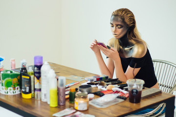 Model is playing mobile phone during a break and waiting for a makeup artist.