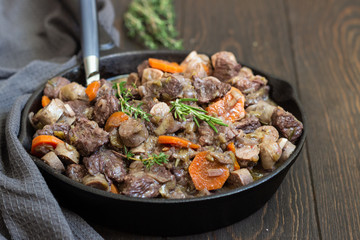 A skillet with beef bourguignon or meat stewed with sausages, carrots, garlic, onion, red wine, fresh herbs and spices.