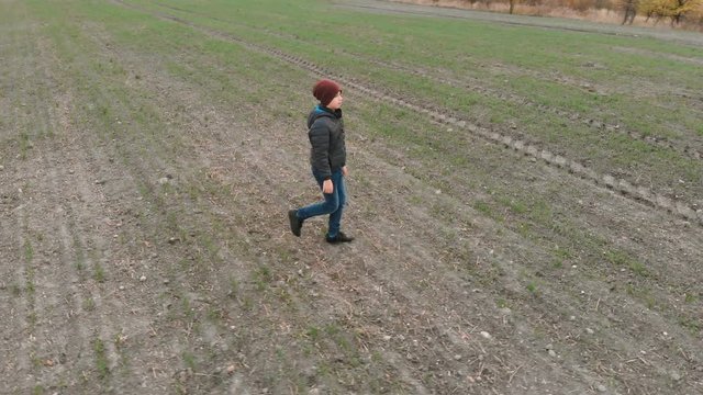 The lonely boy wanders in autumn in an empty, plowed, gray field. The croaker is looking for something in the field. The boy is running and walking.