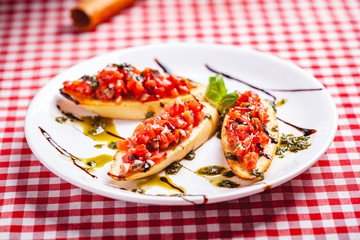Traditional Italian bruschetta with cherry tomatoes, pesto sauce and balsamic vinegar on white plate. Close up