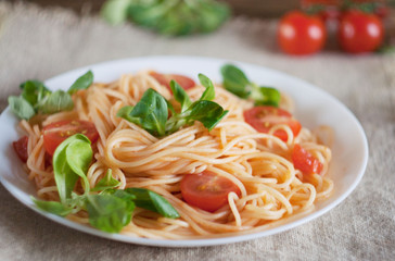 pasta in a plate on a wooden table .. under a plate napkin of flax. near cherry tomatoe