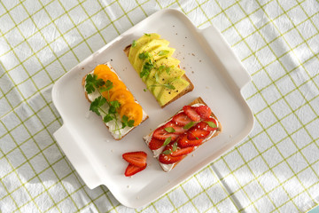 Breakfast: Toast with strawberries, avocado and yellow cherry tomatoes on a plate, top view