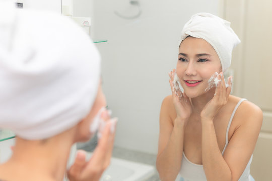Woman happy cleanses the skin with foam on sink.