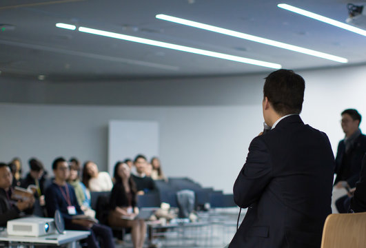 Seminar Audience in Training Room Watch Presentation. Speaker in Meeting at Business Event. Expert Presenter Giving Talk with Young Group of People. Rear View of Audience People Who Listen to Speaker.