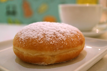Obraz na płótnie Canvas One strawberry jam filled doughnut with blurred white coffee cup in background 