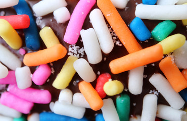 Macro shot of colorful sprinkles on chocolate glazed doughnut for background or banner 