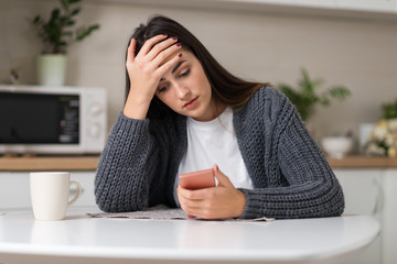 Stressed woman reading something on her cell phone at home