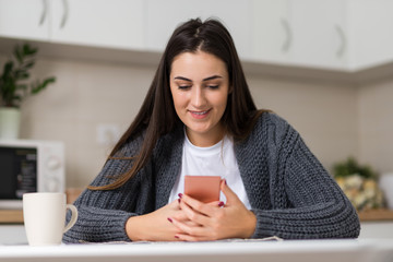 Young smiling woman typing message on mobile phone at home